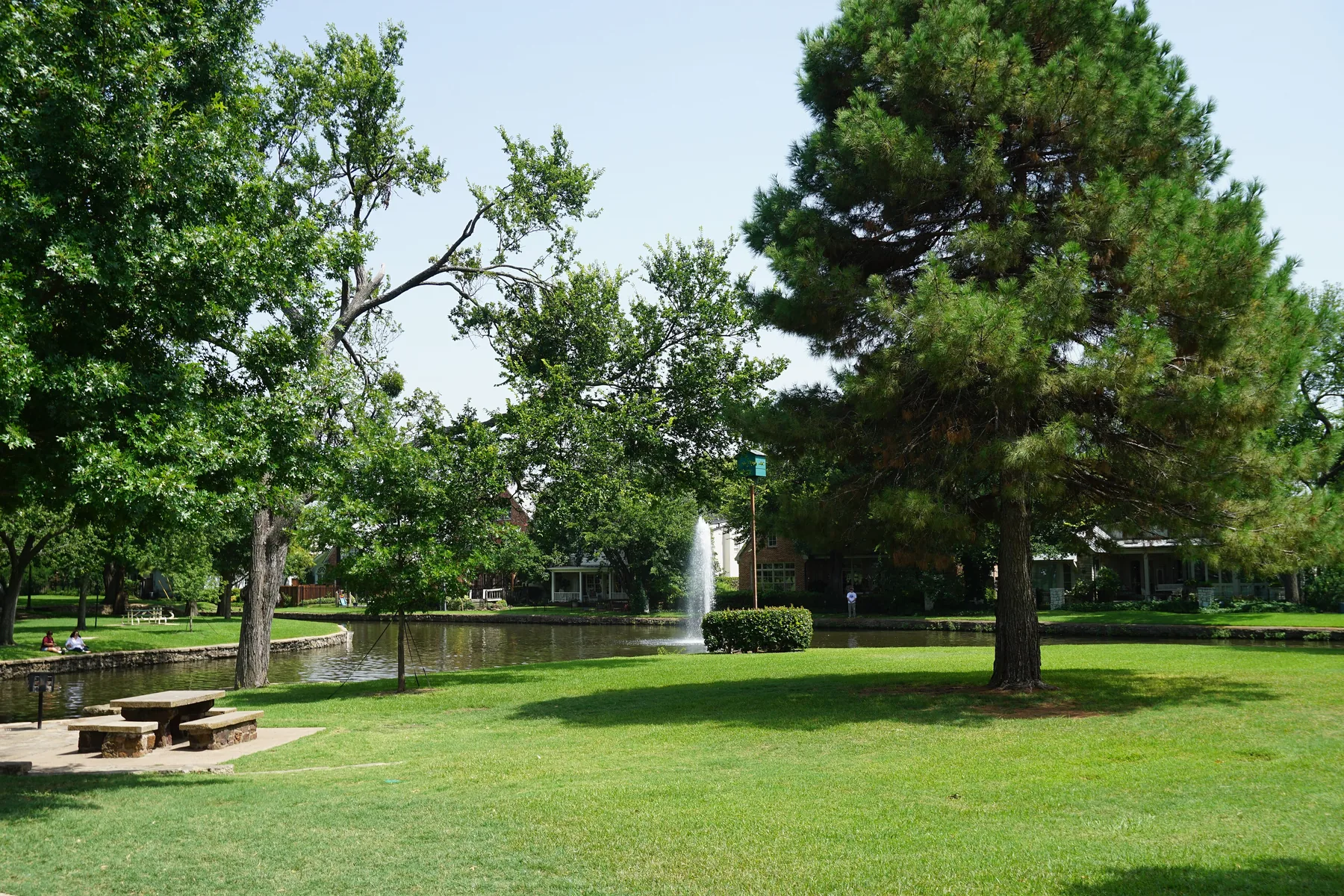 Pond with a fountain under tall pines at Caruth Park in University Park, Texas